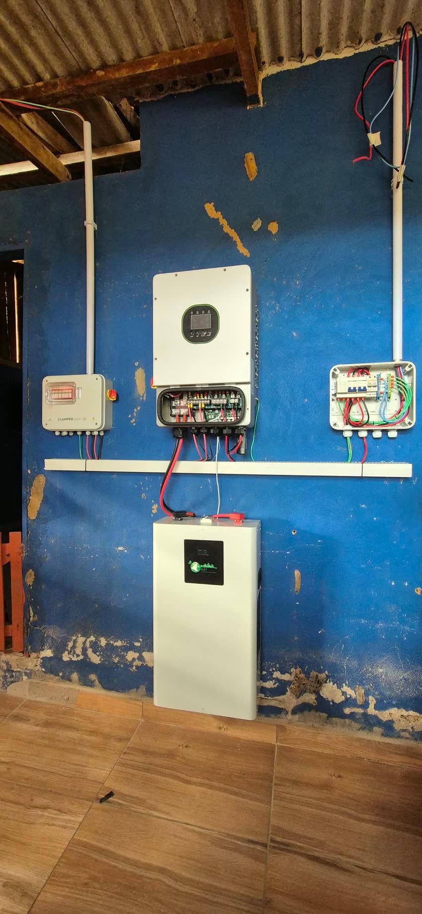Inversor híbrido e quadro de proteção instalados em parede azul