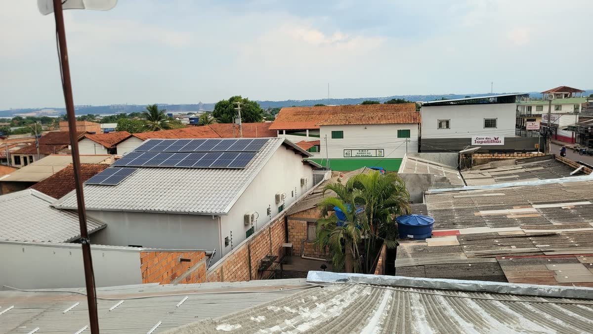 Módulos fotovoltaicos instalados em telhado residencial, com o bairro ao fundo